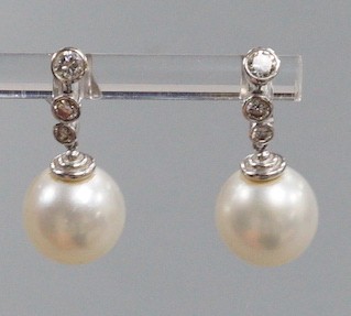 A modern pair of 750 white metal, singe stone South Sea pearl and graduated three stone diamond set drop earrings, overall 22mm, gross weight 6.8 grams